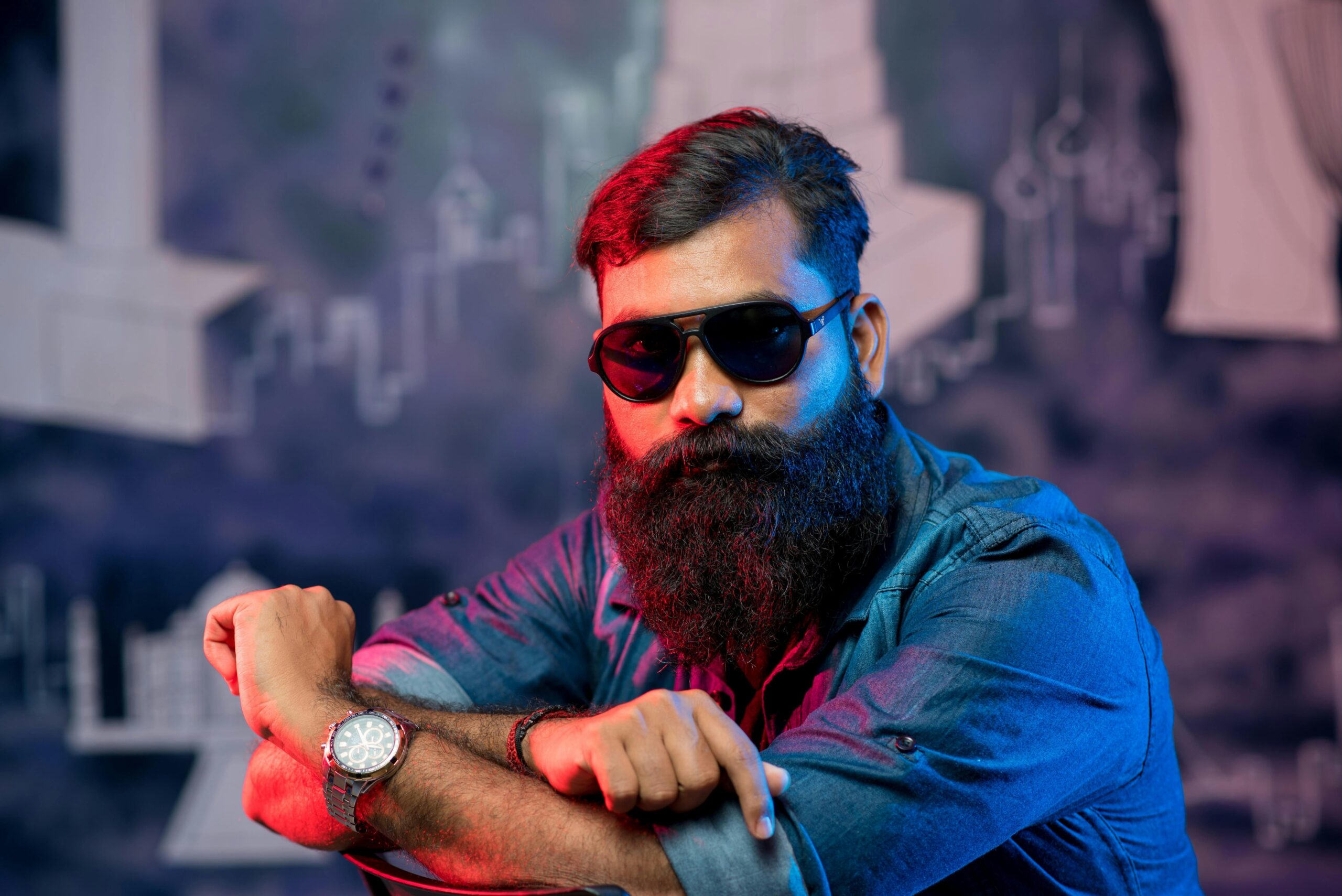 Portrait of a fashionable man in sunglasses and beard posing confidently in a studio setting.